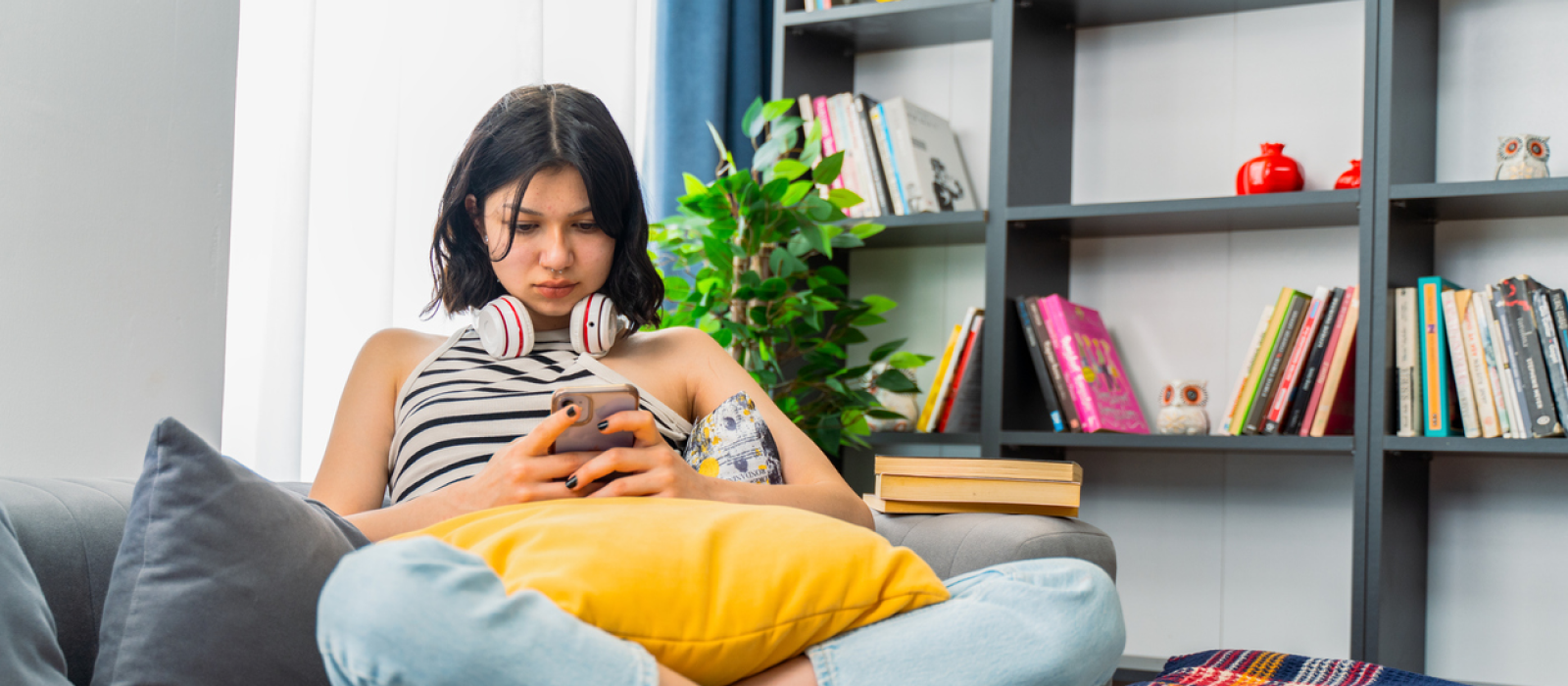 A young female sits at home on her couch. She is scrolling on social media.