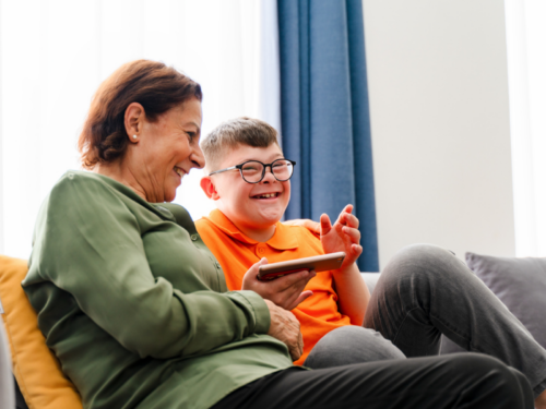 A mom and her son sit on their couch laughing. Her son has a disability and December 3rd marks International Day of Persons with Disabilities.