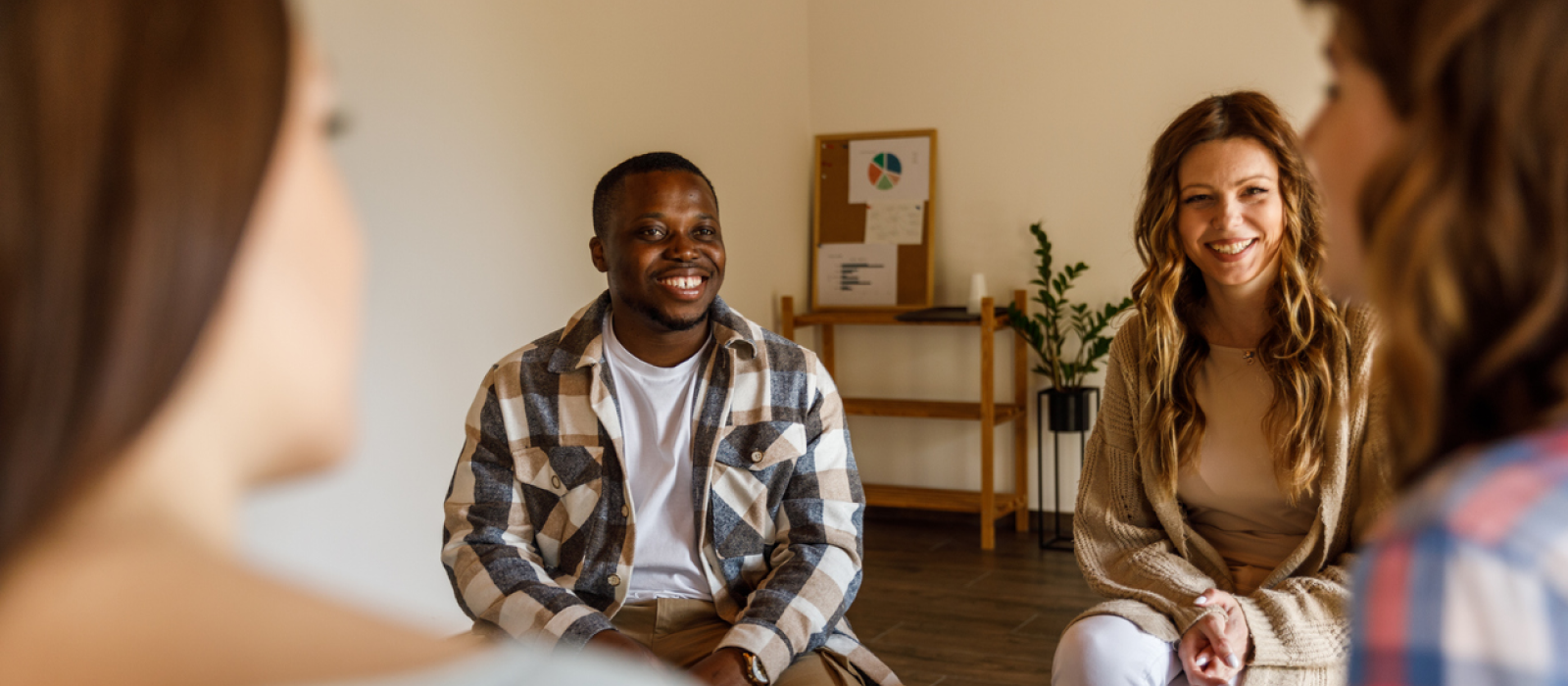 A man and woman are pictured sitting with their support group. They are in a peer support group to help them help a loved one with a substance abuse problem.