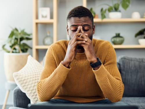 A young male sits on his couch with his head in his hands. He has been in chronic pain and it has been brutal for his mental health.