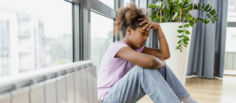 A young teenager sits on the floor in her room. Chronic pain has been brutal for her mental health.