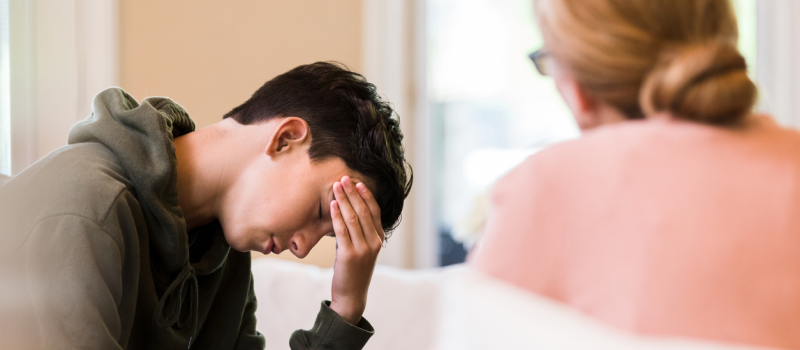 A young male sits with his mother in their living room. Alcohol is affecting his mental health and his mother is worried about his alcohol use.