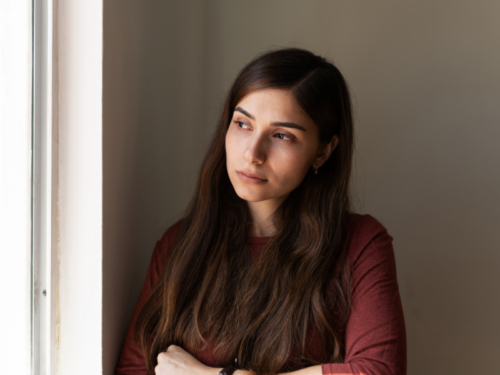 A young woman looks out of the window of her house. She has post-traumatic stress disorder (PTSD).