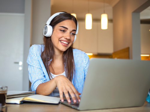 A young woman in a blue top and white headphones at her computer. She is in virtual CBT therapy.