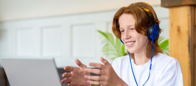 A young teen with red hair and a white shirt at their computer. The teenager is in virtual DBT therapy.