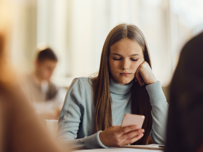 A teen holds her phone and is digitally self-harming.