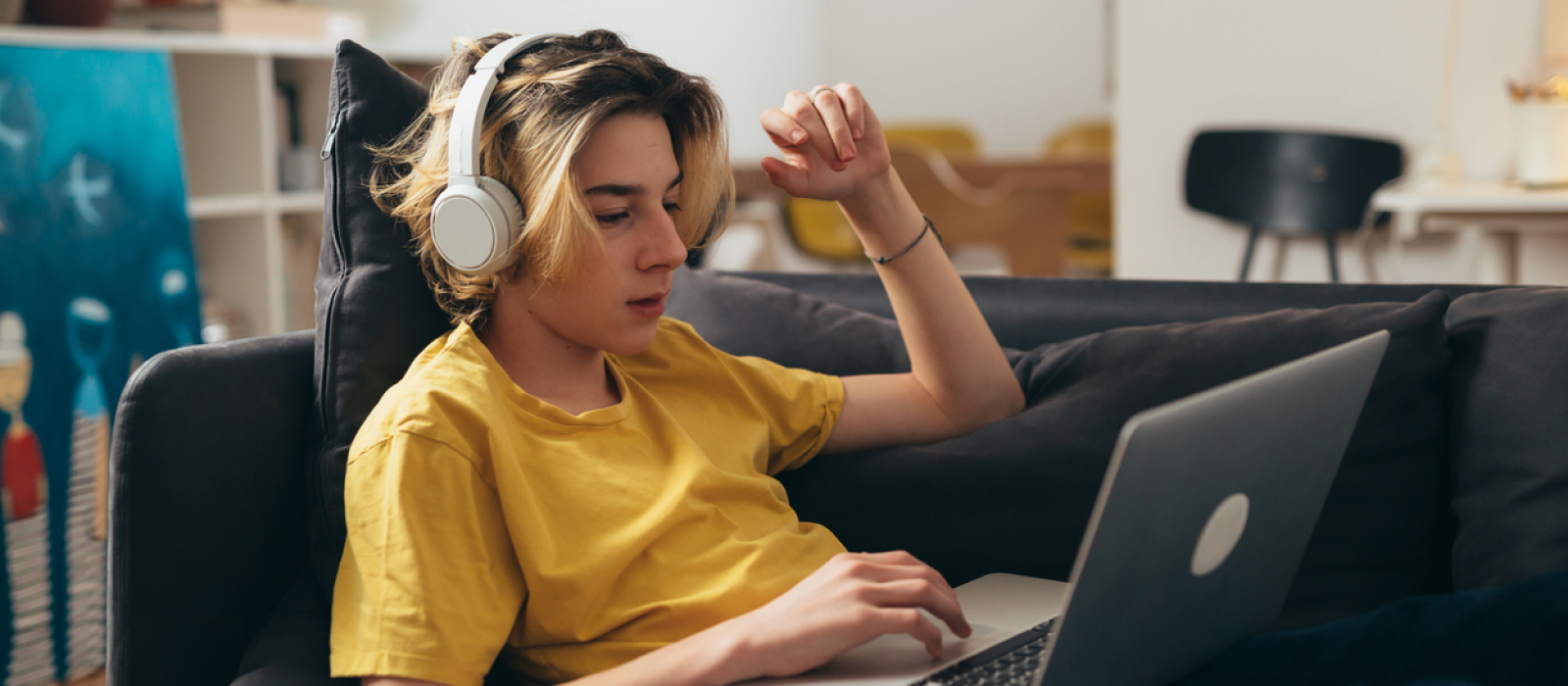 A male teenager in a yellow shirt sits on the couch on his computer. He is in virtual therapy, and is projecting, which is a defense mechanism.