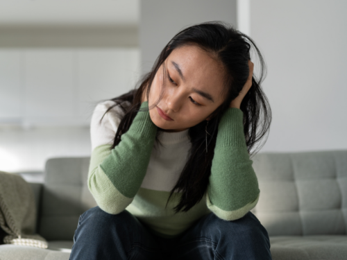 A young woman sits on her couch. She has paranoid personality disorder and is learning how to cope with it.