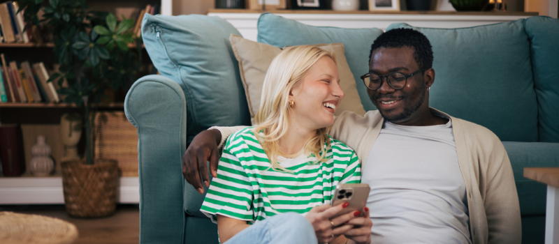 A young couple sits on the ground together smiling.