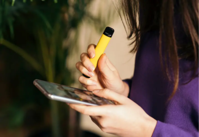 A teen holds a vape scrolling through her phone with anxiety.