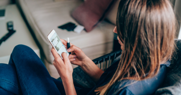 A teen uses a vape while texting on their phone