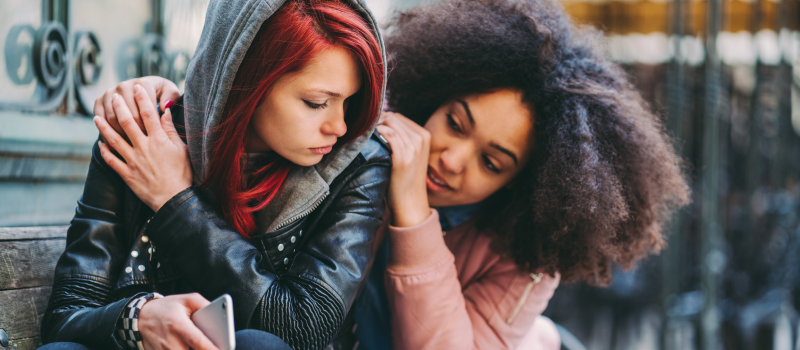 Two teens with the one girl comforting her friend by giving her a hug