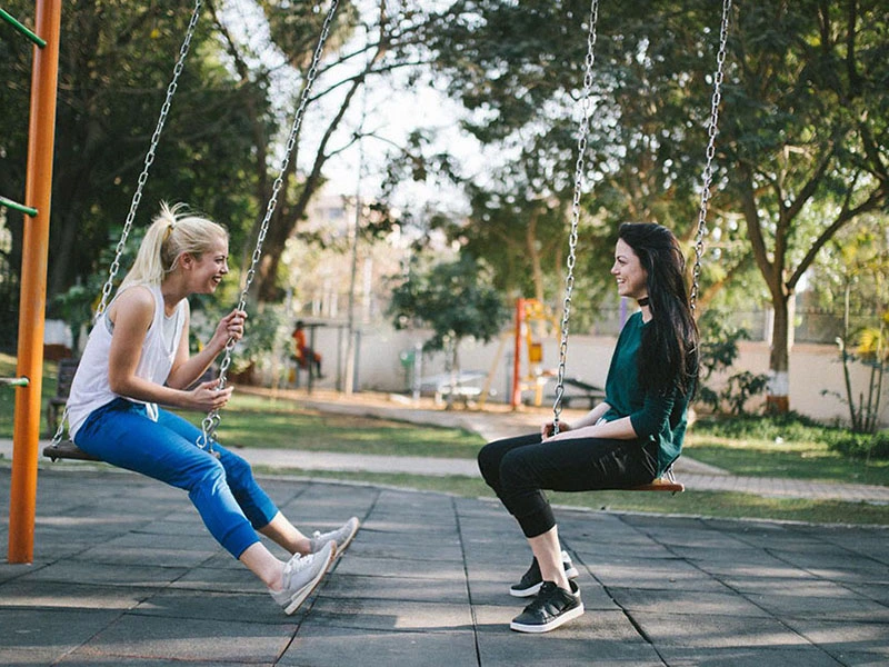 Friends chatting while sitting on a swing set