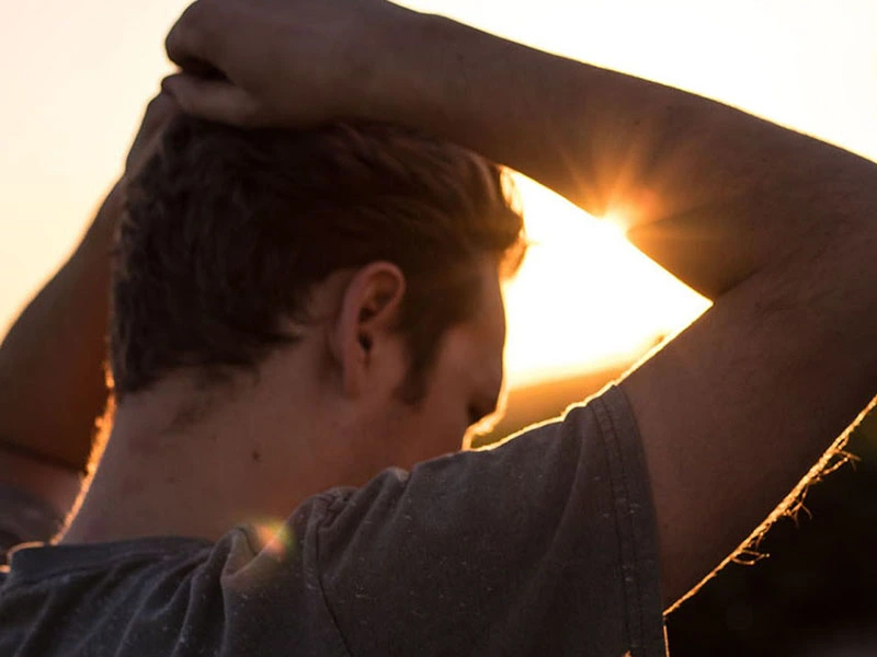 Man looking depressed as he stares at the ground while the sun is setting