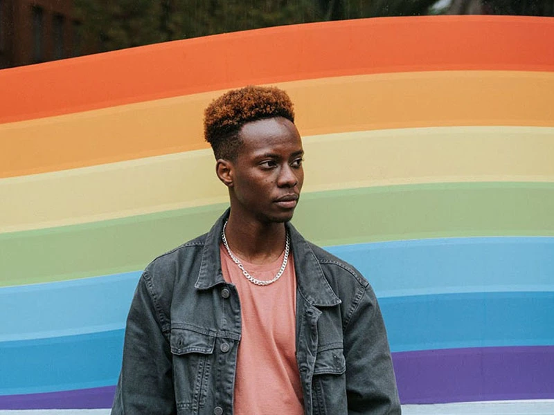 A young man stands in front of a Pride flag