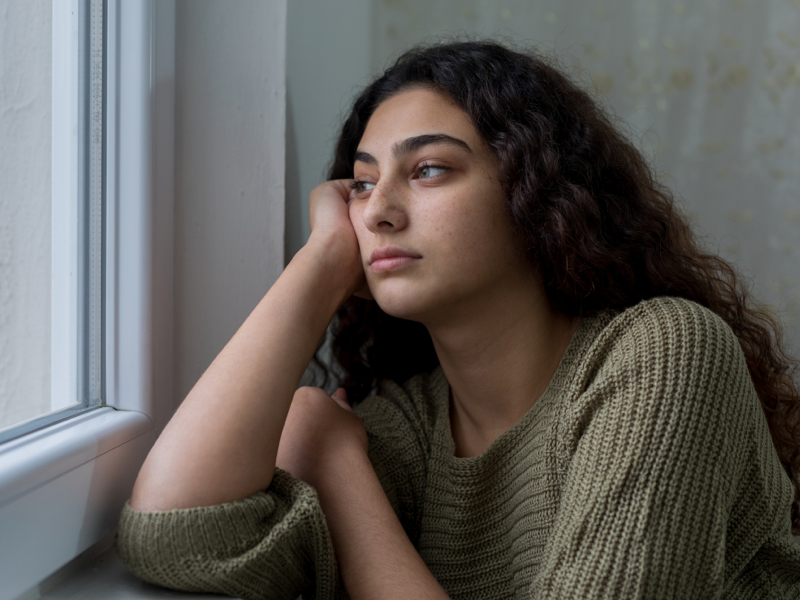 Teen dealing with mental health issues alone looking out a window