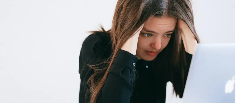 A teen sits with her hands in her hair staring at her laptop