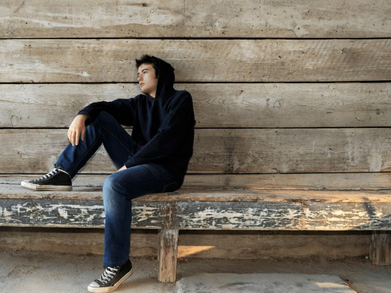 Male teenager sitting on a wooden bench alone looking lonely