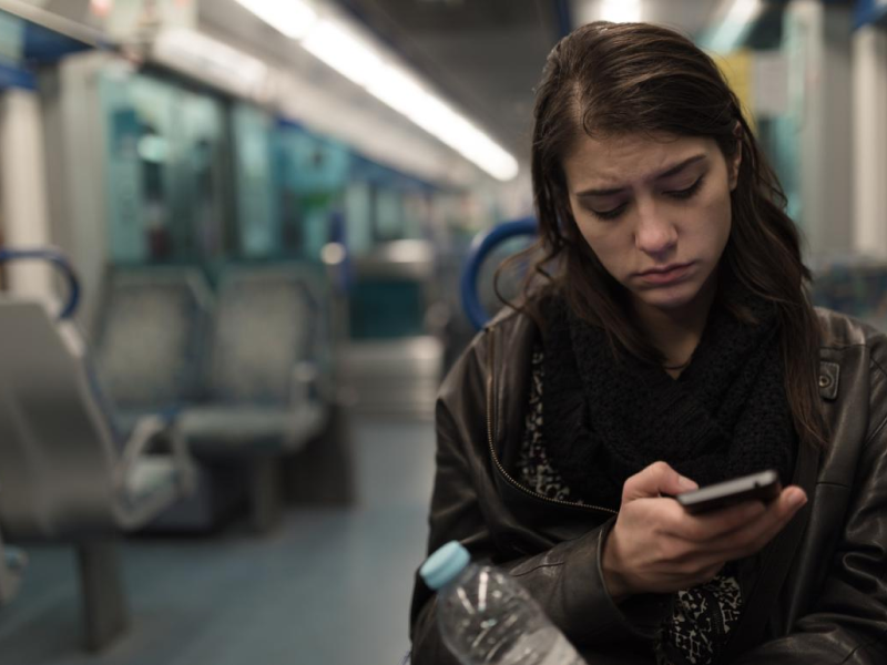 A young person using their phone while sitting alone and looking sad on the train