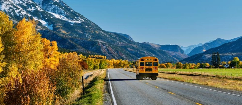 school bus driving on a road with mountains in the background in Colorado