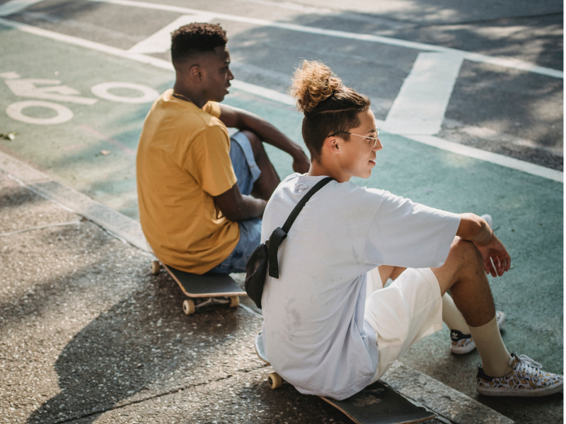 Two teen boys sit on a sidewalk talking about their mental health