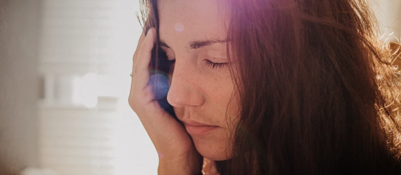 A young adult female with brown hair who needs therapy sits with her head in her hand