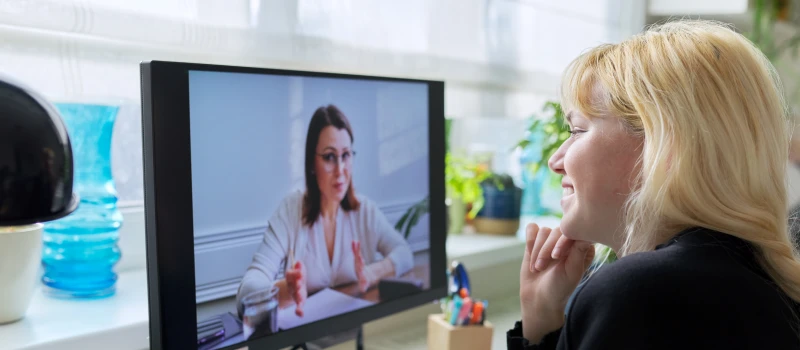 A teen girl with blonde hair sits on her computer during a virtual IOP session 