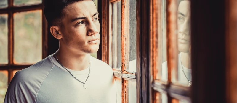 A young man stares of a window thinking about treatment options for complex trauma