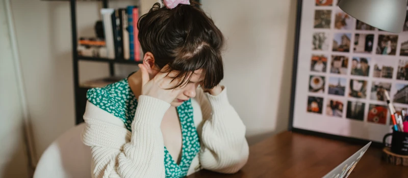 A young woman in a green dress is anxious and sits with her head in her hands