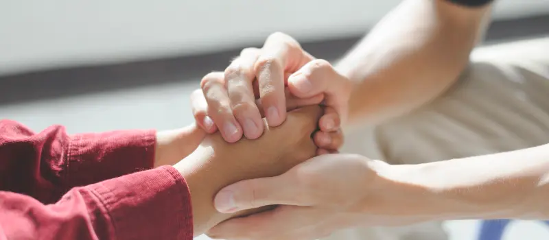 A friend holds the hand of another friend who's struggling with trauma