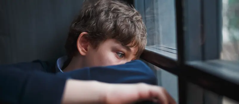 A young boy dealing with mental health issue stares out of his window