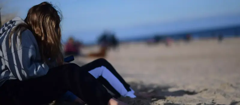 Teen on popular beach looking at sad at her phone