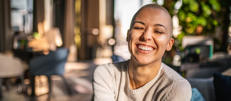 A young woman with a shaved head is smiling because she is secure in her relationships
