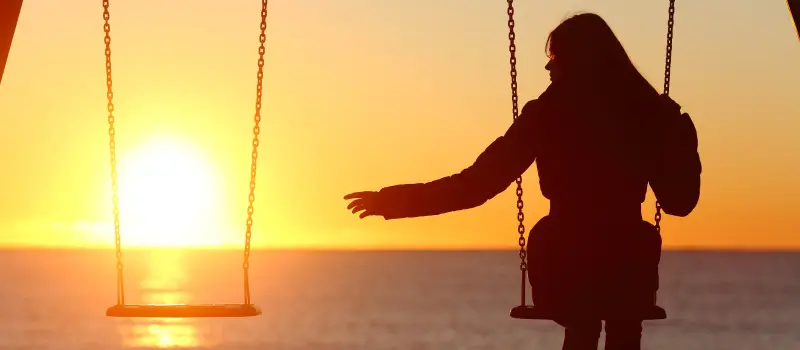 A teen girl processing grief sits alone on a swing set at sunset