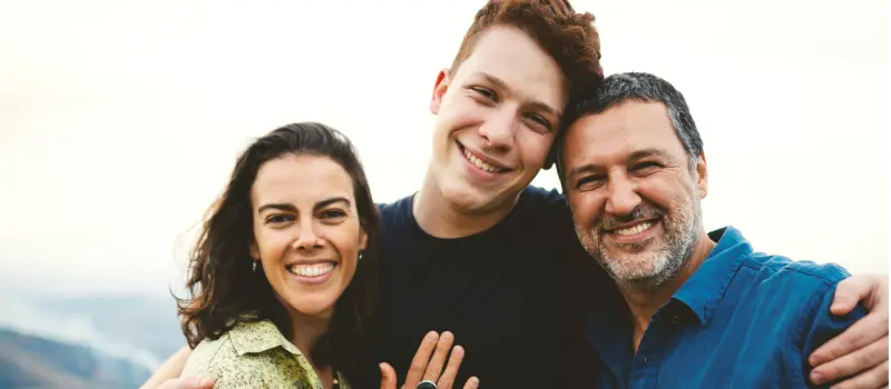 A mother and father hug their teen son whose mental health is improving through IOP