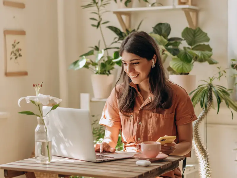 A young woman sits at her dining room table smiling while looking into joining an intensive outpatient program