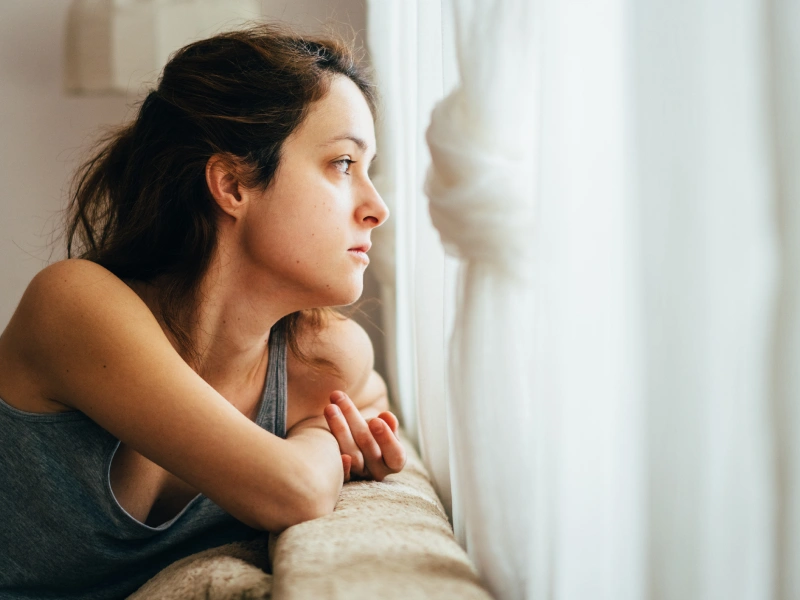 A young woman who feels out of her body stares out of her bedroom window