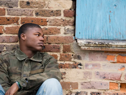 A young man in a camouflage coat sits on the group processing grief and trauma