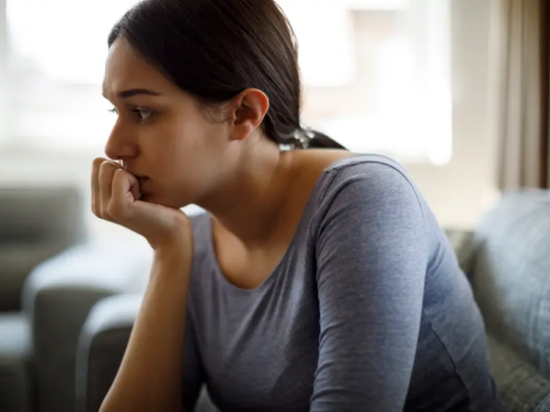 A young woman sits on a couch struggling with a phobia of growing up