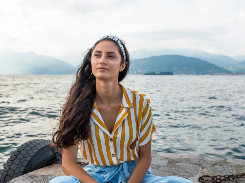 A young woman with a secure attachment style sits on a peer by a lake looking off into the distance