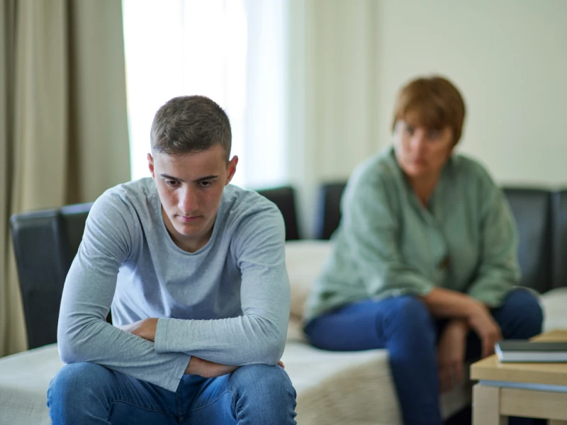 A young teen male sits with his back toward his mother avoiding conflict