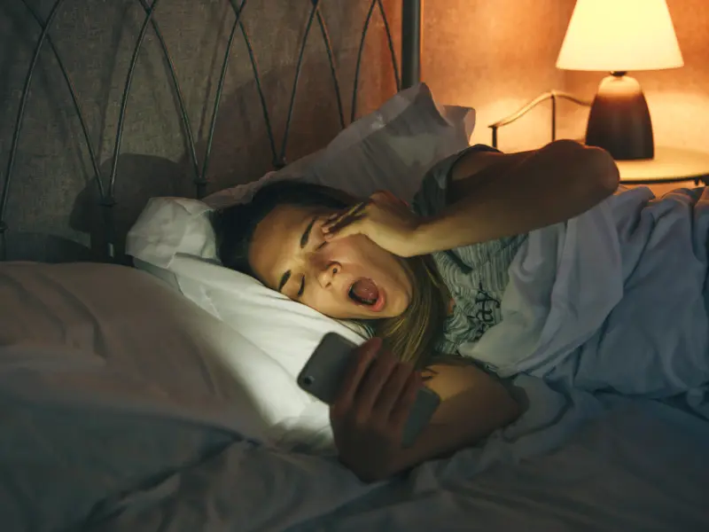 A teen girl dealing with depression lays in bed on her phone