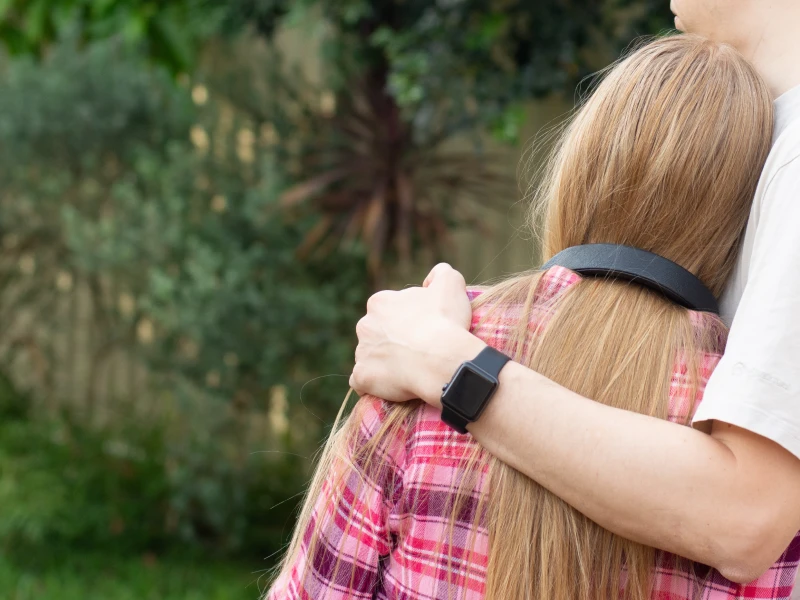 A father stands with his arm wrapped around his teenage daughter