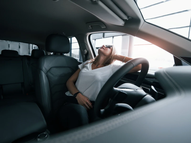 A young woman sits in her car with head sticking out of the window
