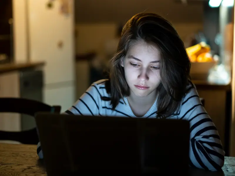 A teen with acute stress disorder sits at her laptop in the dark
