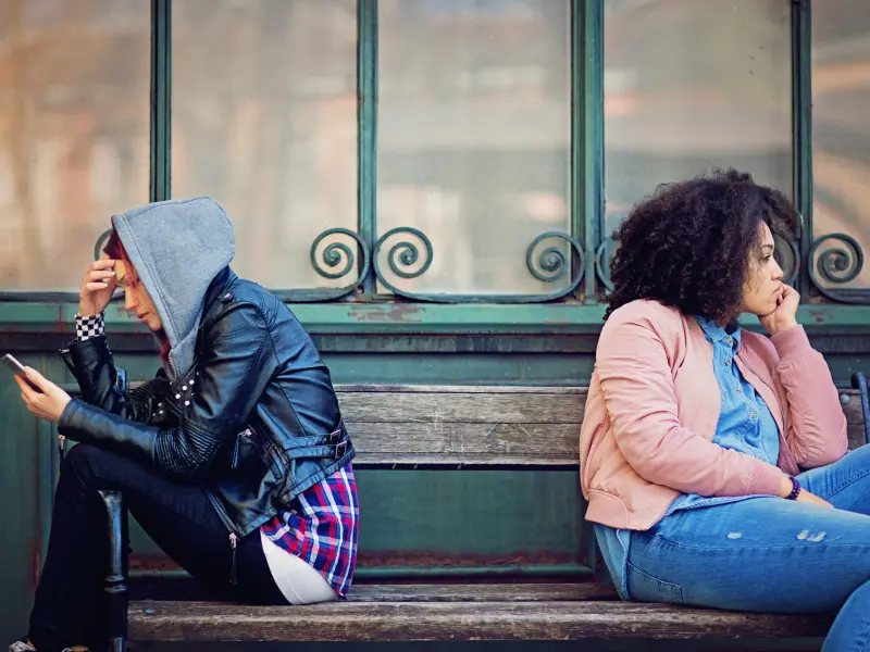 Two teens sit with their backs to each other