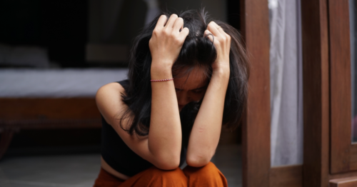 Young woman sits with her head in her hands