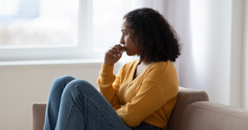 A young woman struggling with serious mental health issues sits by and stares out of a window