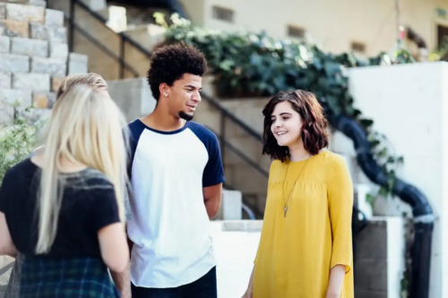 A Black male teen and a white female teen stand together talking about looking at things from the positive side
