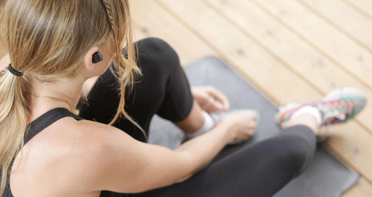 Teen girl sitting down tying her shoes to go workout for self care.